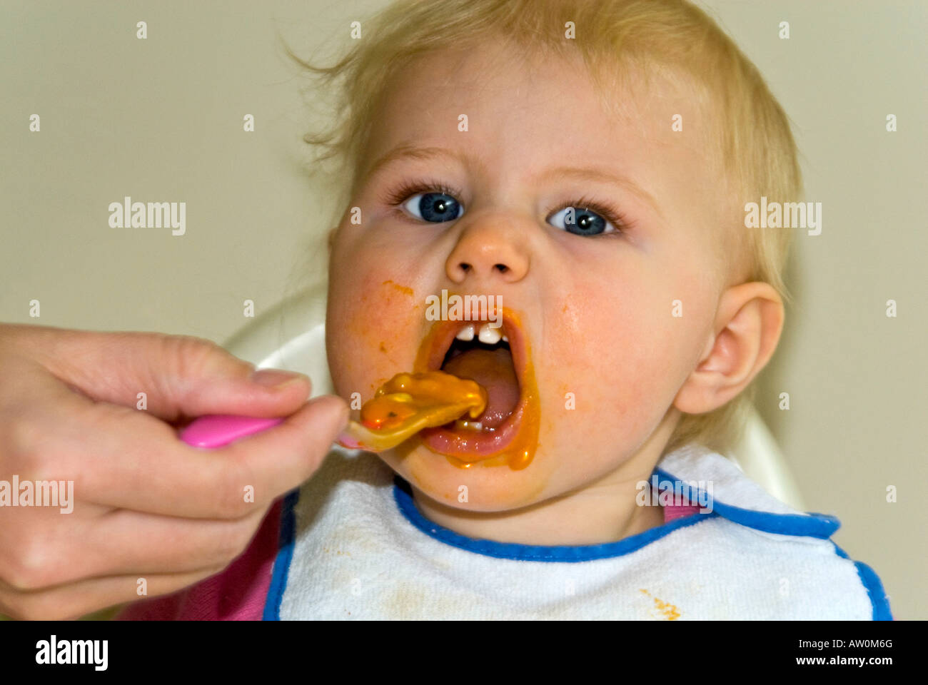 Horizontal close up of a pretty Caucasian baby girl in a high chair at dinner time with food all over her face Stock Photo