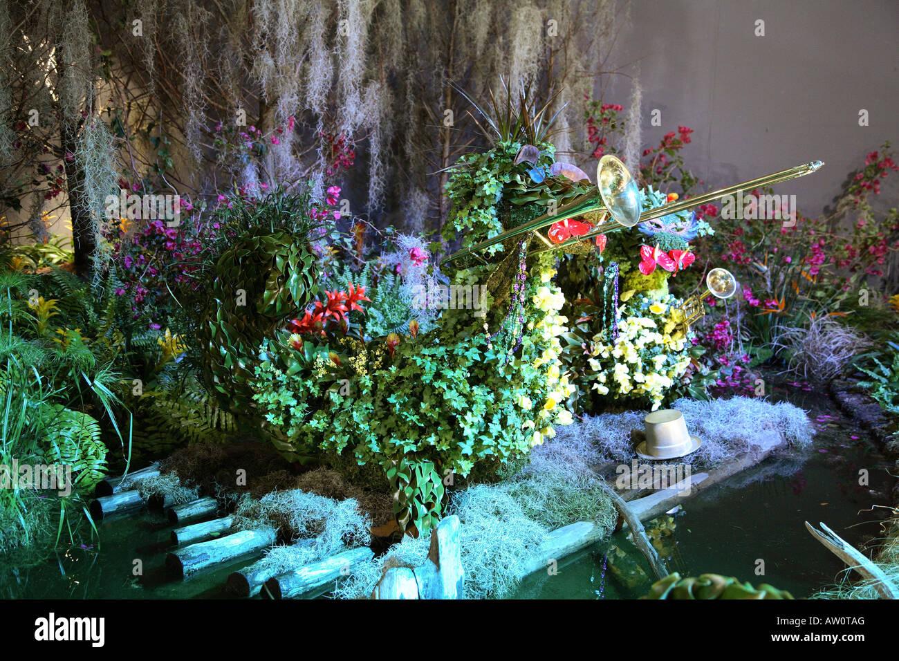 Topiary alligator trombone player. Body made of pansies, magnolia leaves ivy and moss.  Standing on logs in small pool of water Stock Photo