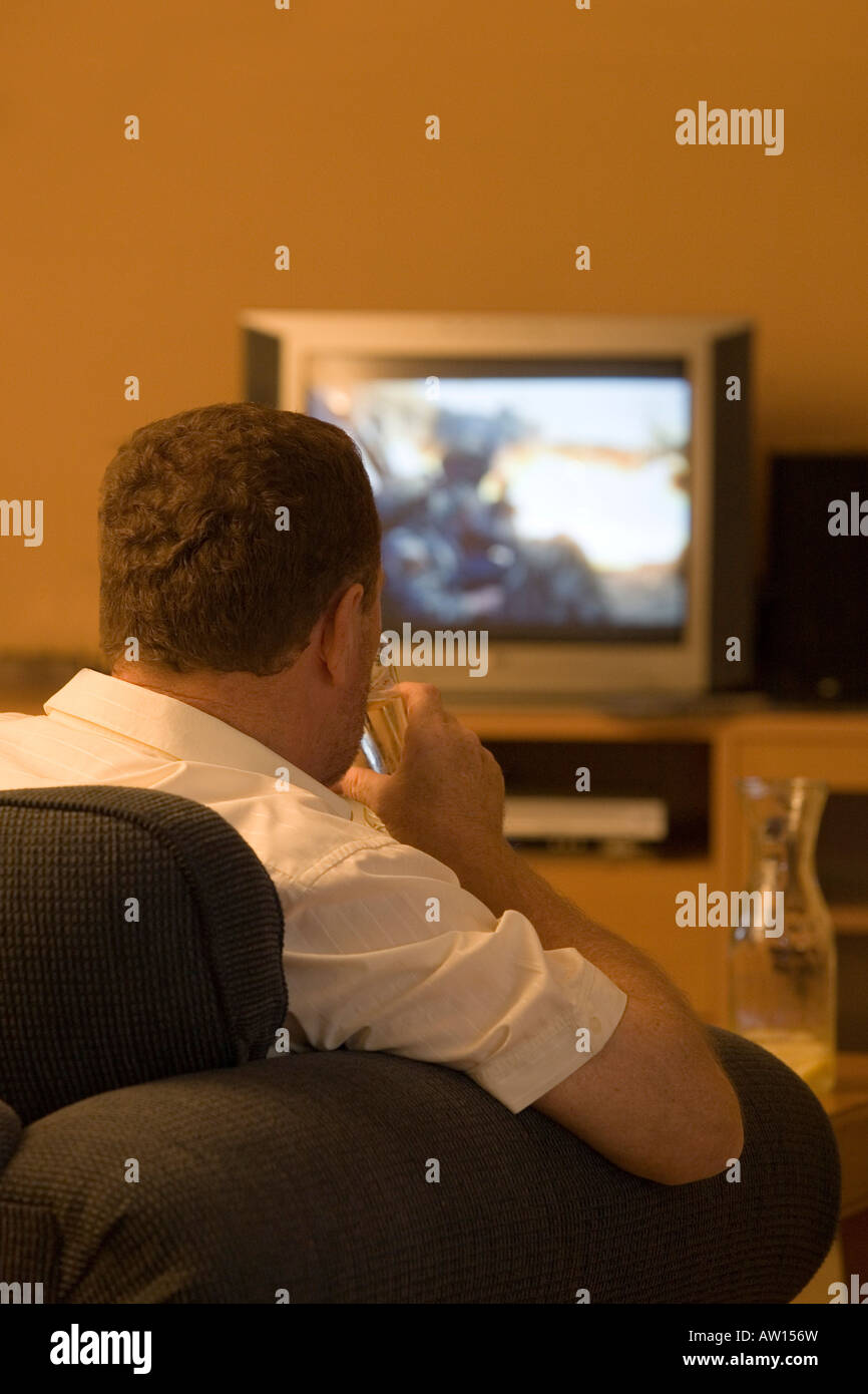 TV Violence. A man watching war film on a television. Hes drinking liquid in a glass. Stock Photo
