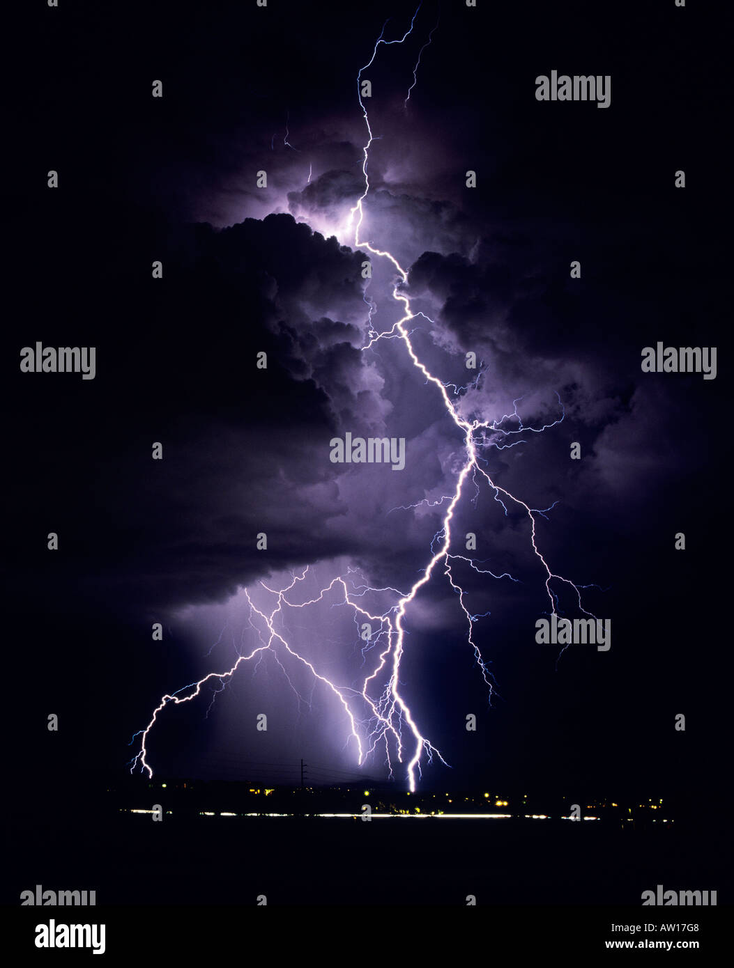 Lightning bolts strike dramatically from a dark and stormy sky. The clouds glow purple and are ominous against the dark night. Stock Photo