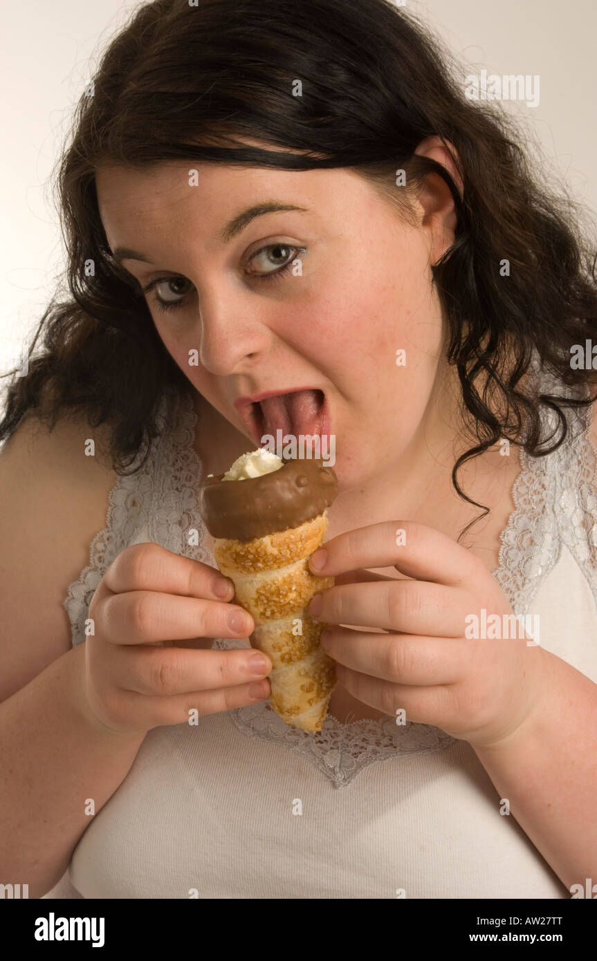Fat overweight young woman guiltily eating a chocolate cream horn Stock Photo