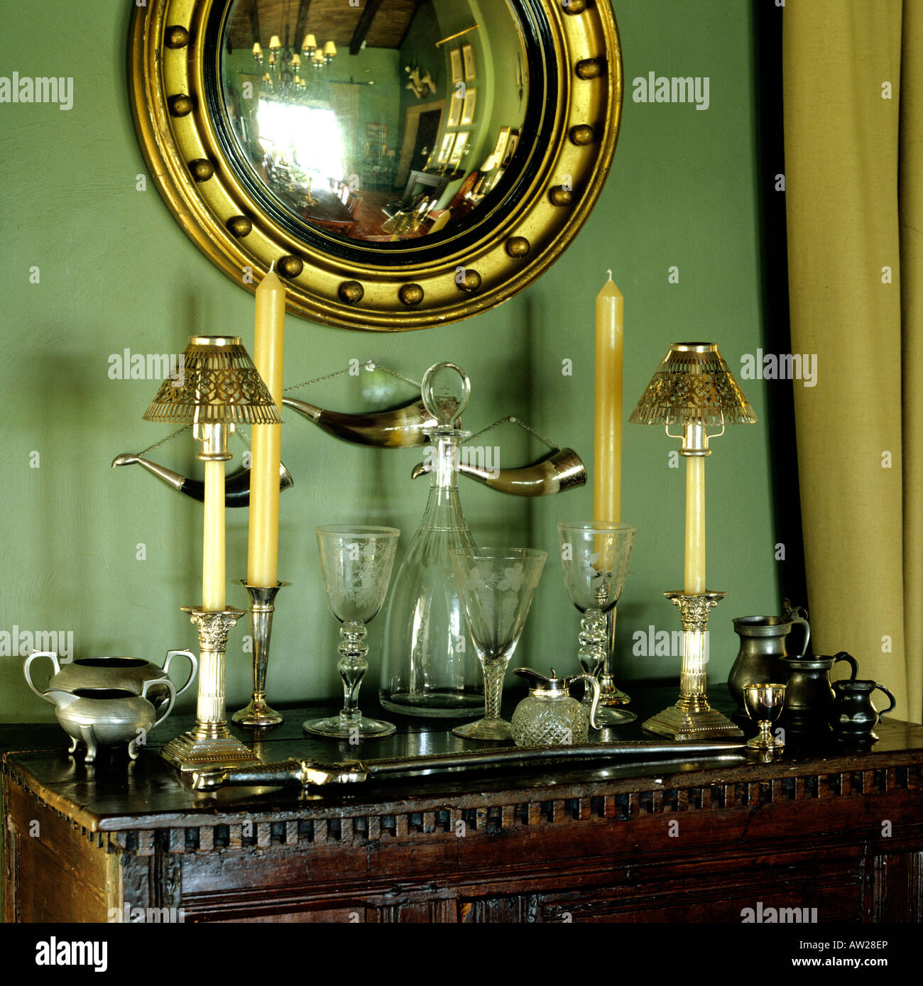 detail of candlesticks and glass ware on top of antique cupboard with convex gilt mirror Stock Photo