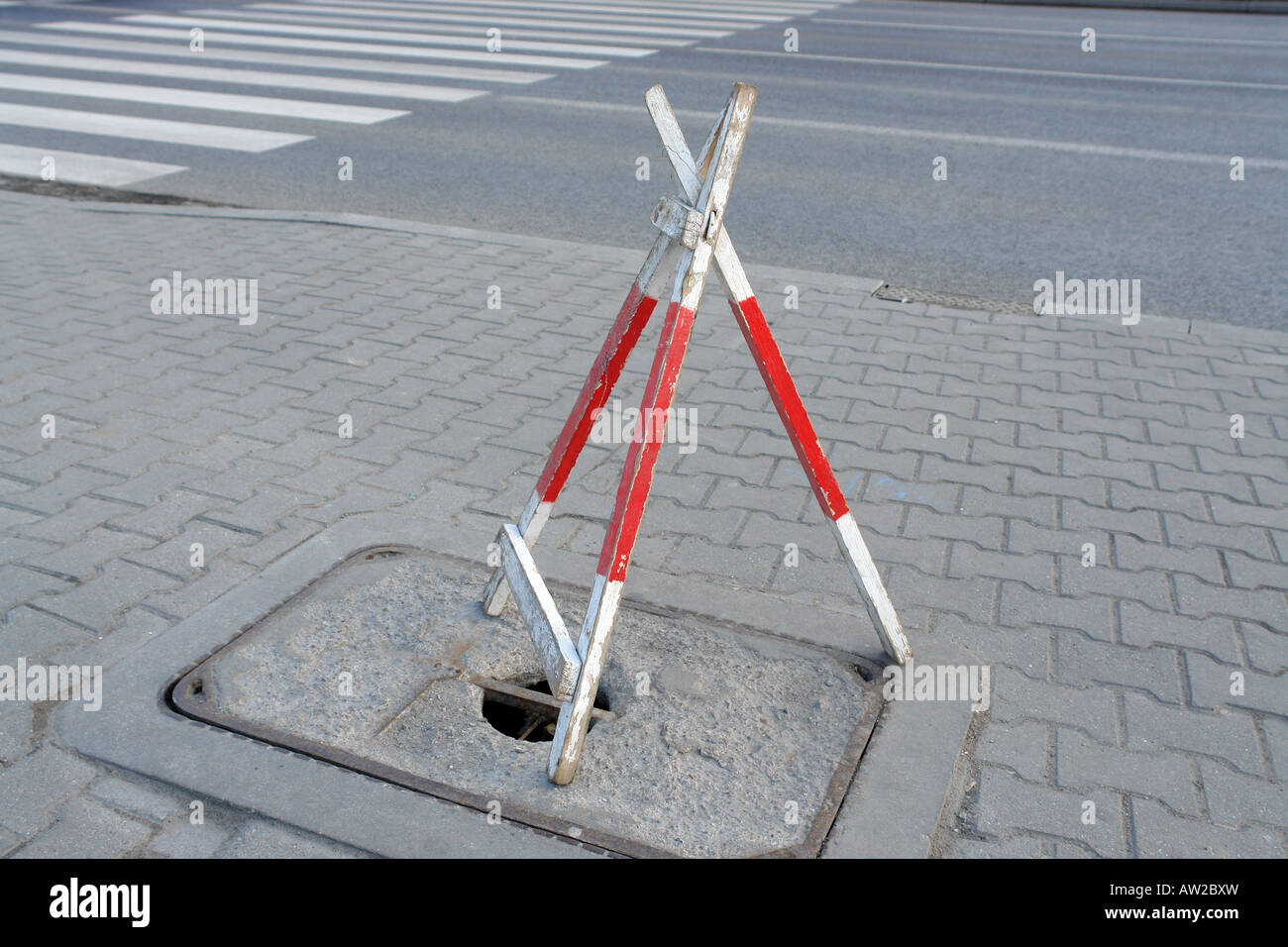 Wooden road tripod barrier placed over hole in sidewalk to protect pedestrians from falling into it Stock Photo