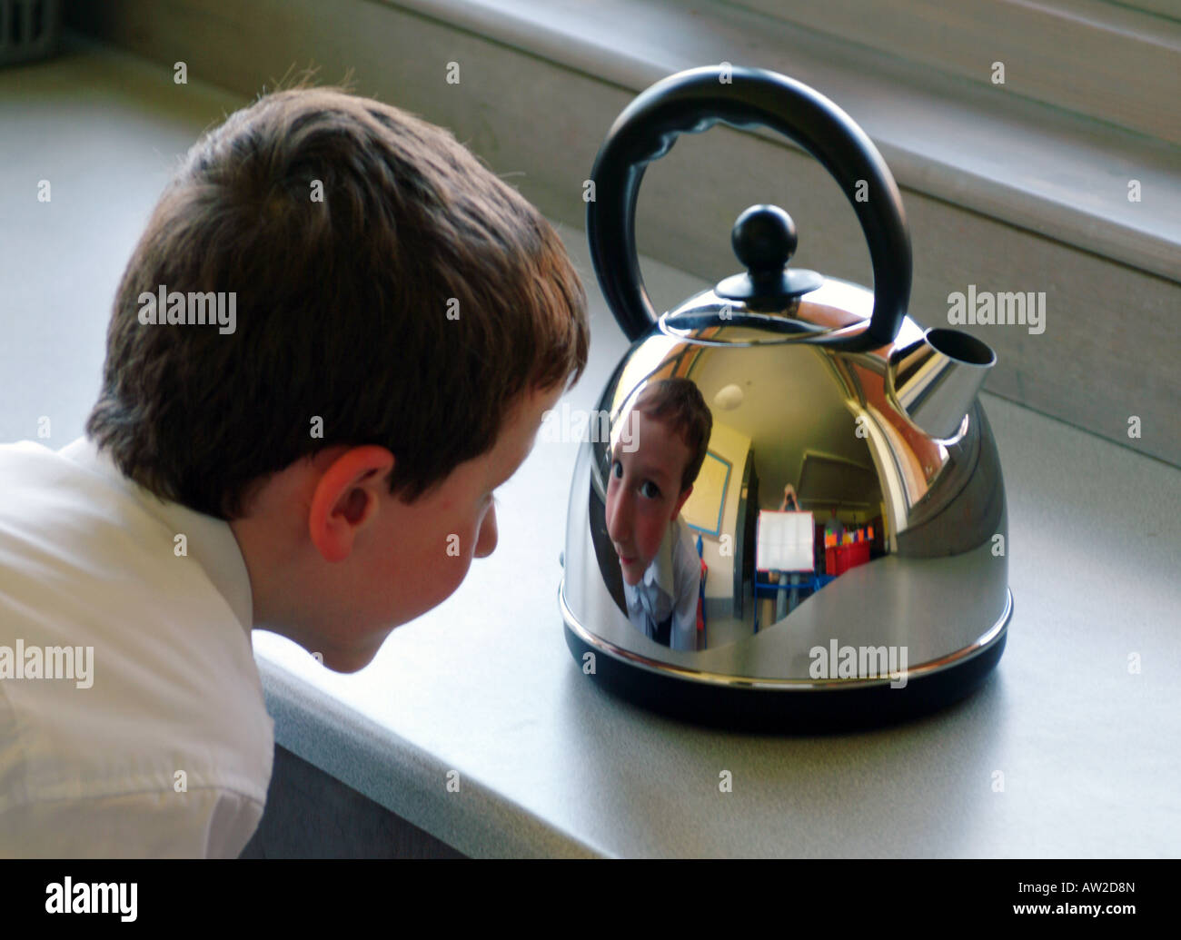 A boy looking at his distorted reflection in a shiny kettle Stock Photo
