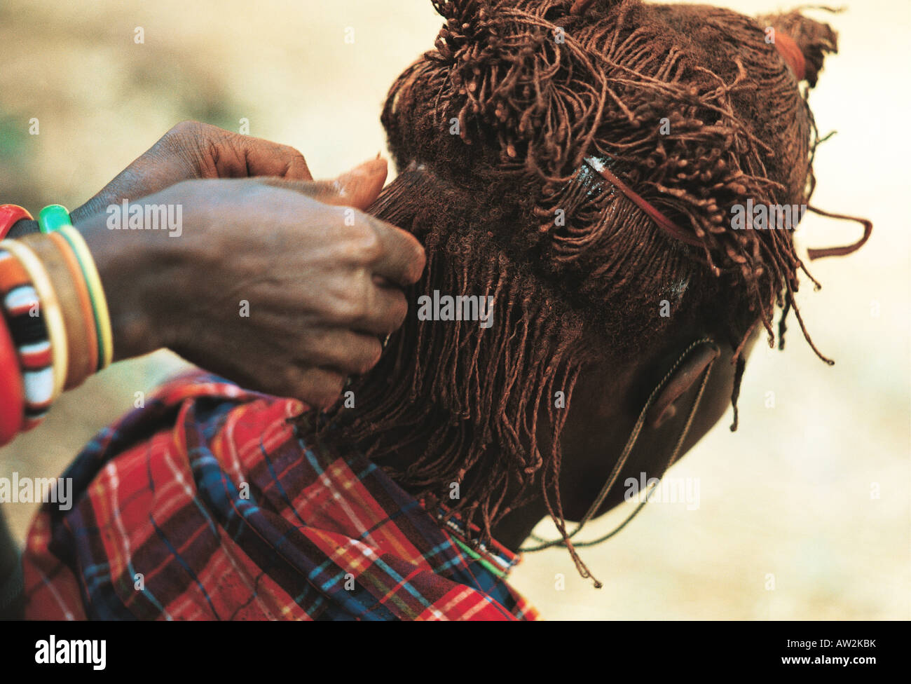 close-up-of-maasai-moran-or-warrior-having-his-hair-braided-and-lengthened-AW2KBK.jpg