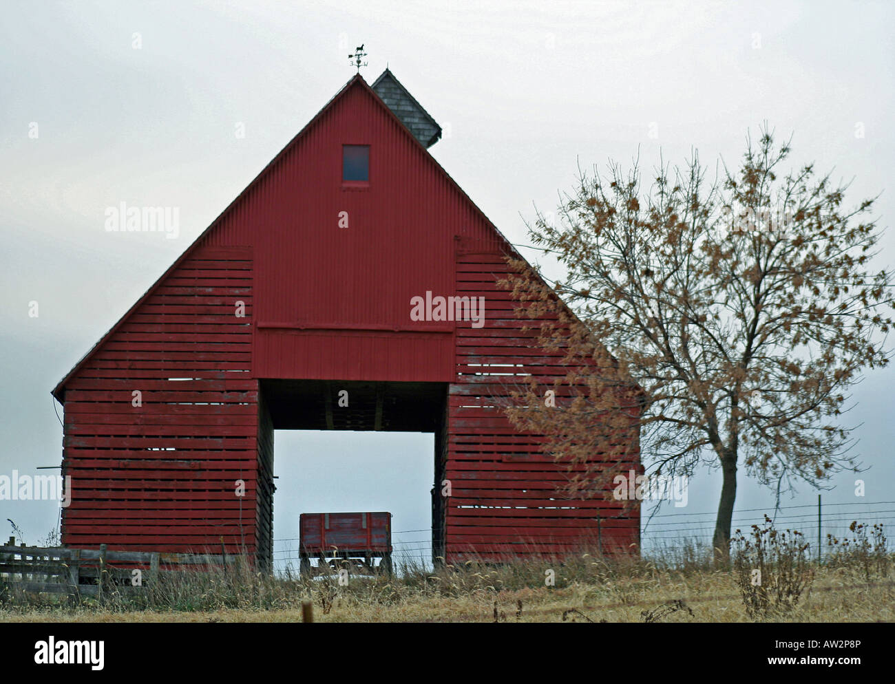 Red corn crib barn on fall day sheltering an old wagon with tree outside with cloud layden sky