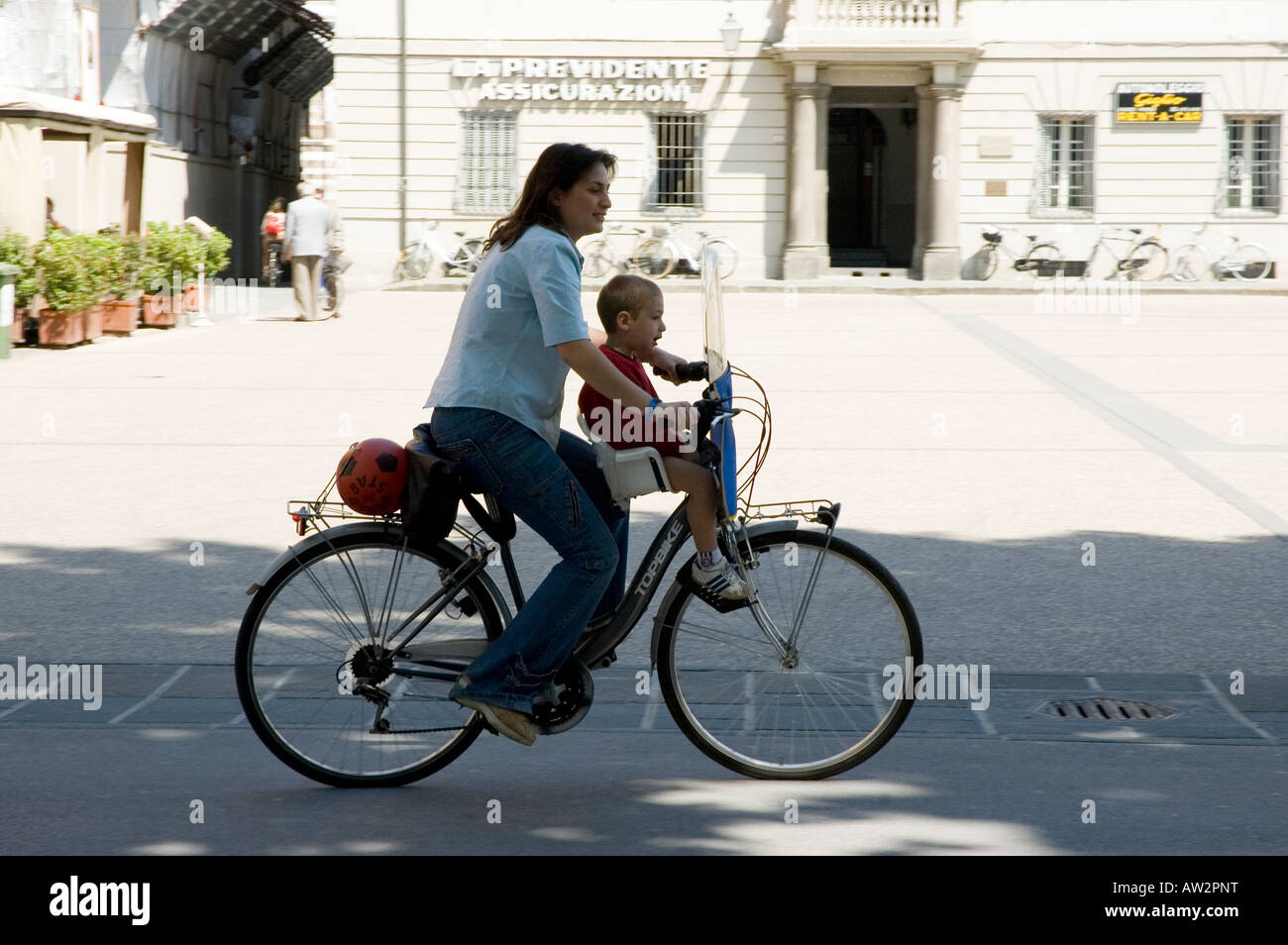 Italian woman riding bicycle with child in seat Stock Photo