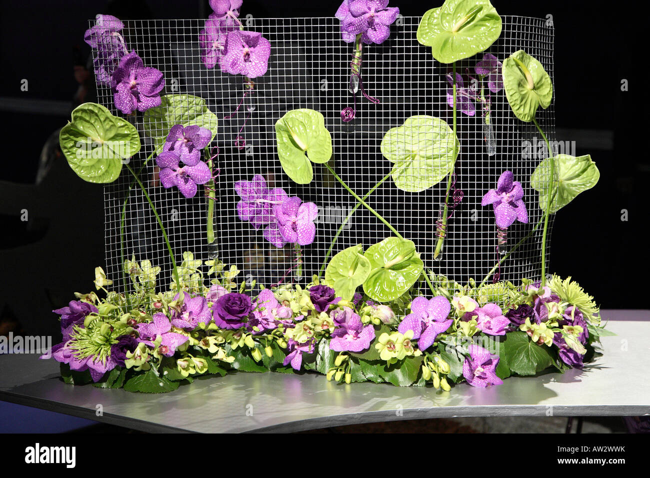 Table arrangement of purple orchids and lime green lilies on wire mesh