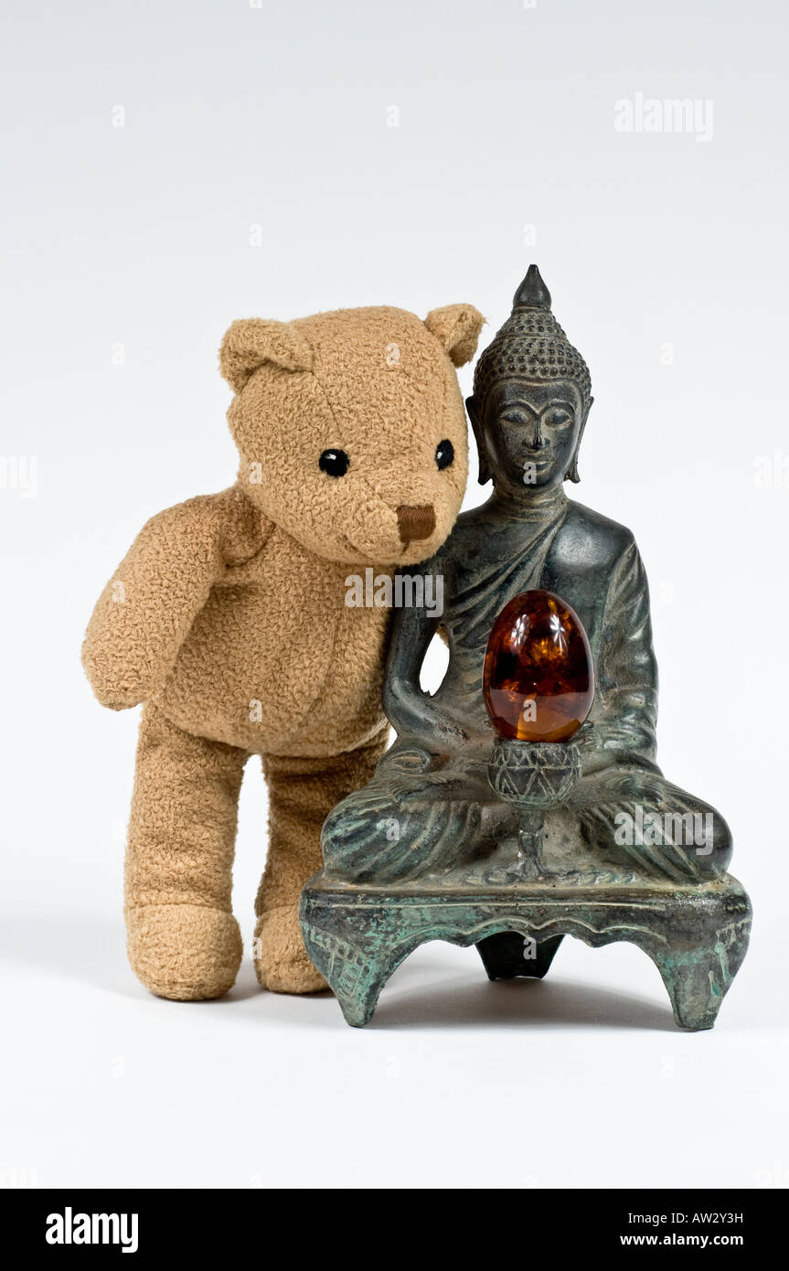 brown stuffed bear looking at a Buddha statue with a amber egg at the center Stock Photo