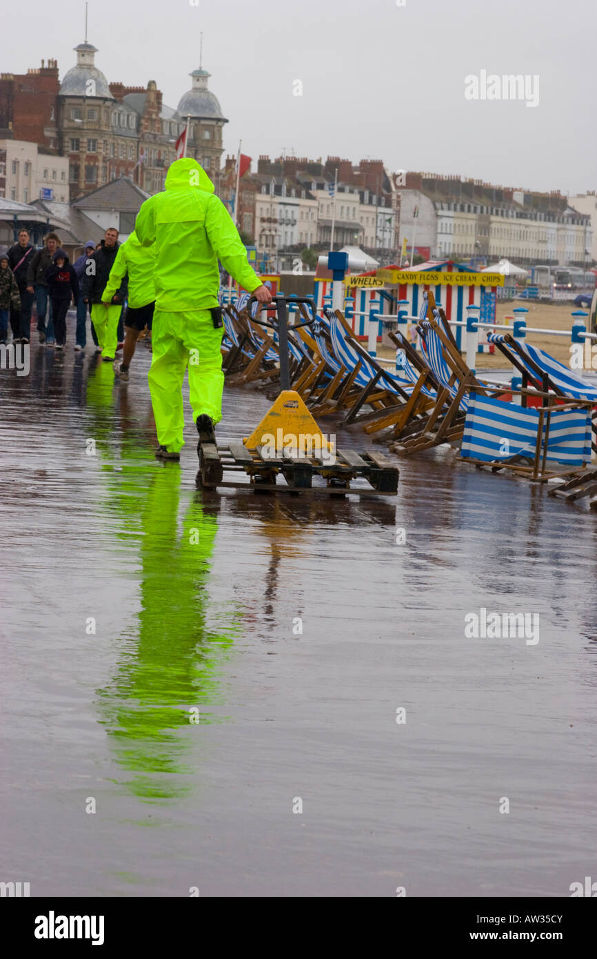 Deck chair attendants in high visibility jackets collect deckchairs abandoned due to wet weather Stock Photo Alamy