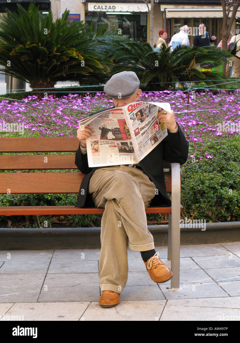 An elderly man reading a newspaper while sat on a bench in a square in, Palma, Mallorca, Spain Stock Photo