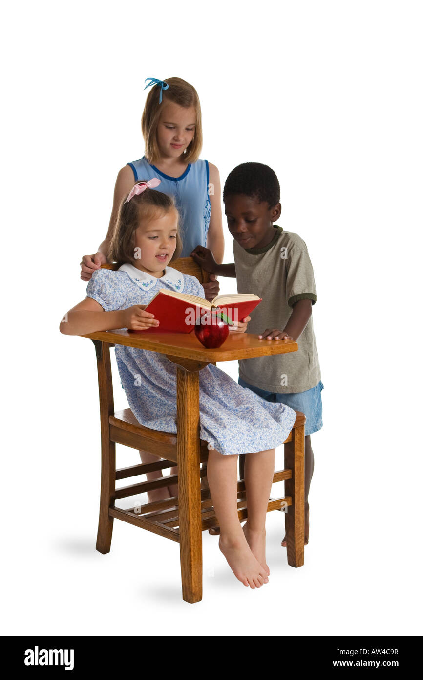 Three young children of different races reading together at a wooden ...
