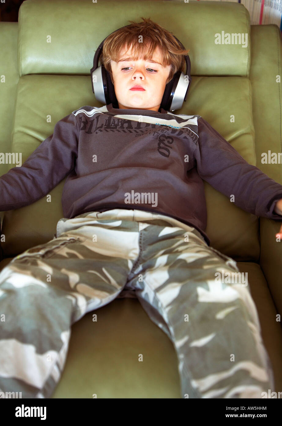 Boy laying back in easy chair listening to music and watching