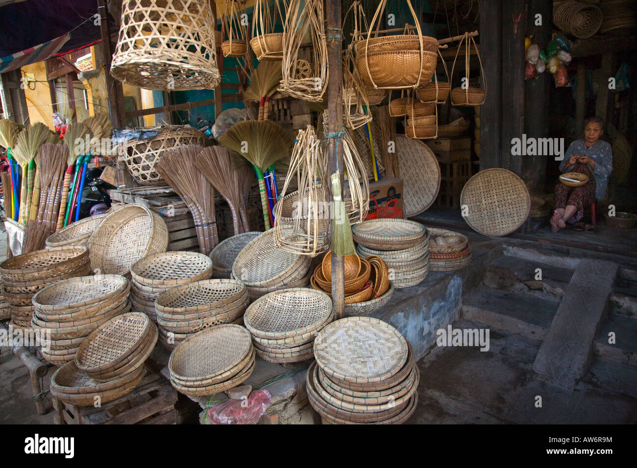 A merchant oversees a large display of WOVEN BASKETS and BROOMS in the village of HOI AN VIETNAM Stock Photo