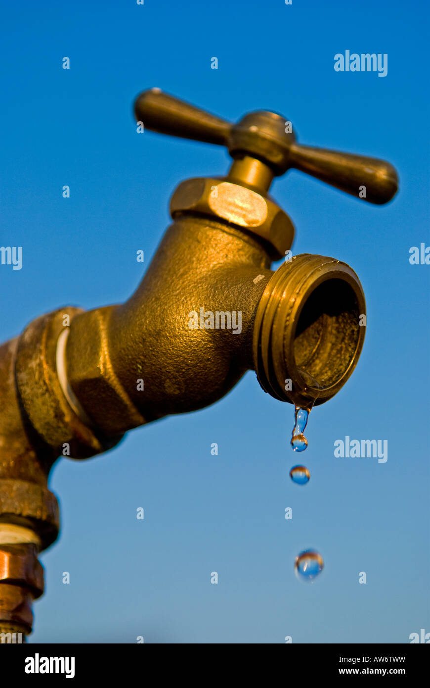 Brass water faucet dripping water - blue sky background Stock Photo