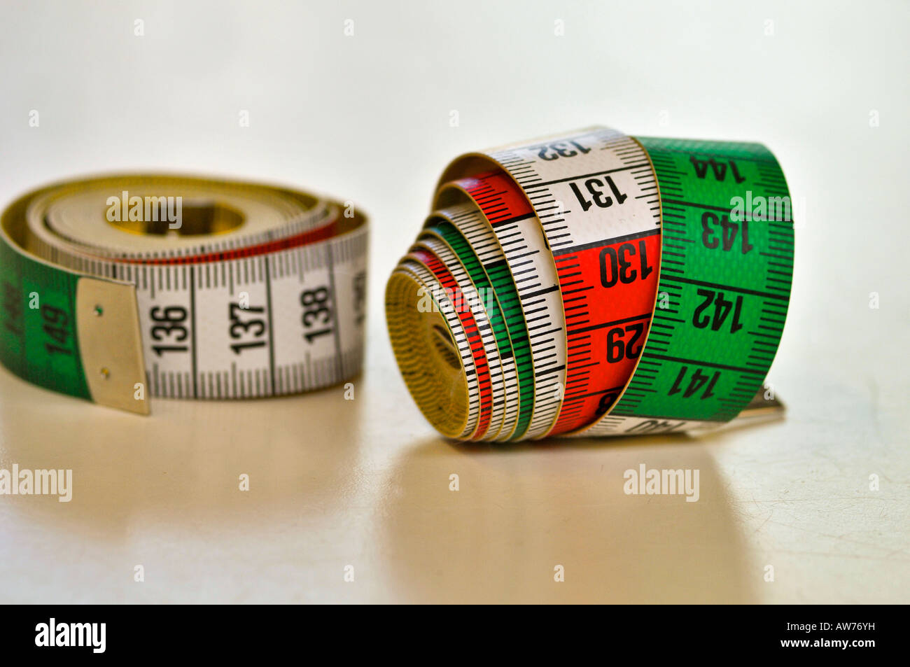 Two tape measure (cm) of seamstress rolled,  resting on a white table. Stock Photo