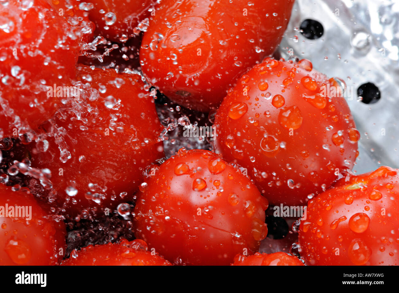 Tomatoes being washed under a jet of water in stainless steel colander