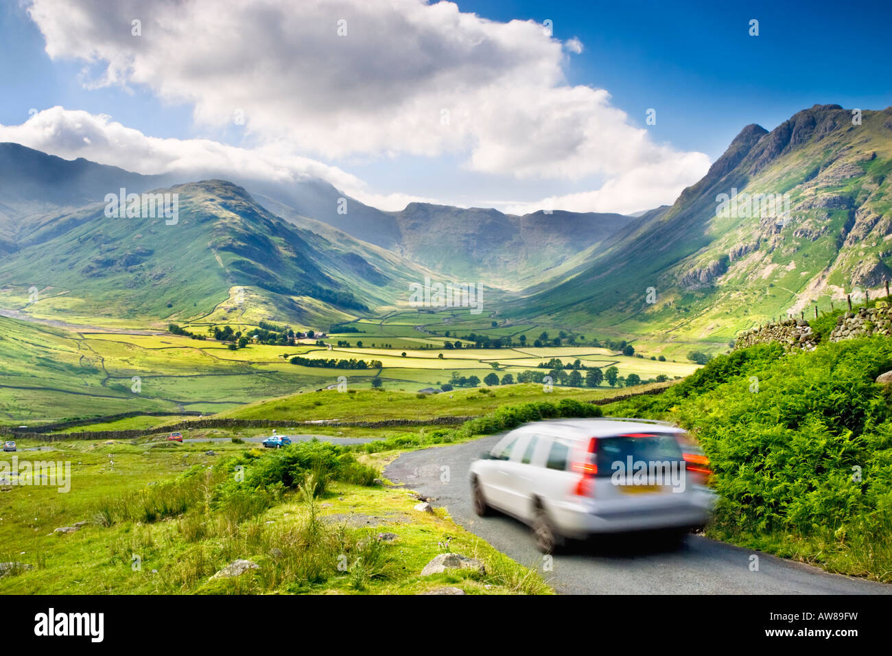 Cars in motion on a countryside road above Great Langdale valley, looking towards The Band, Bowfell and Langdale Pikes. Lake District, UK Stock Photo