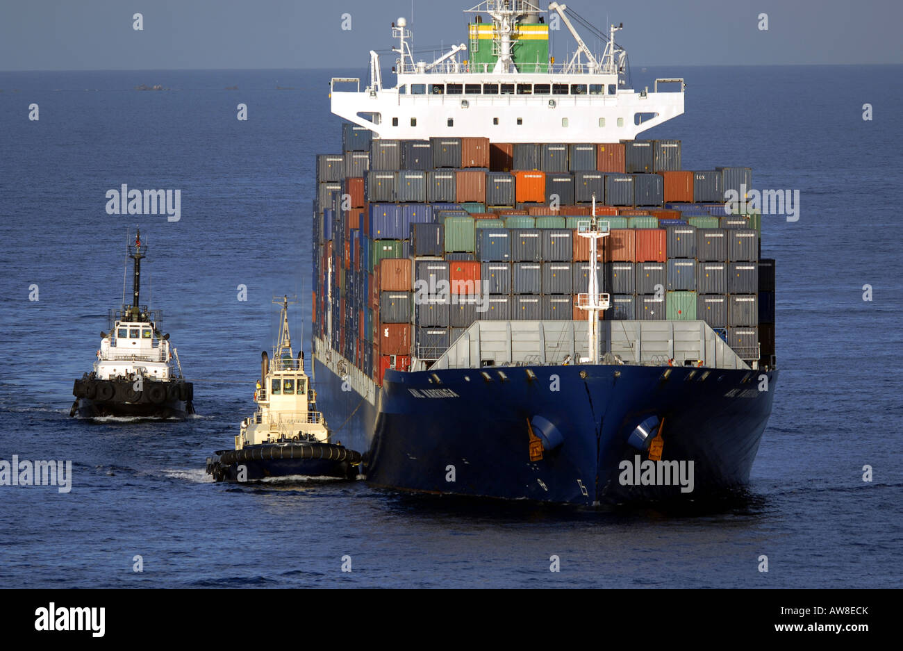 Two small tug boats guide a large container ship into harbour Stock Photo