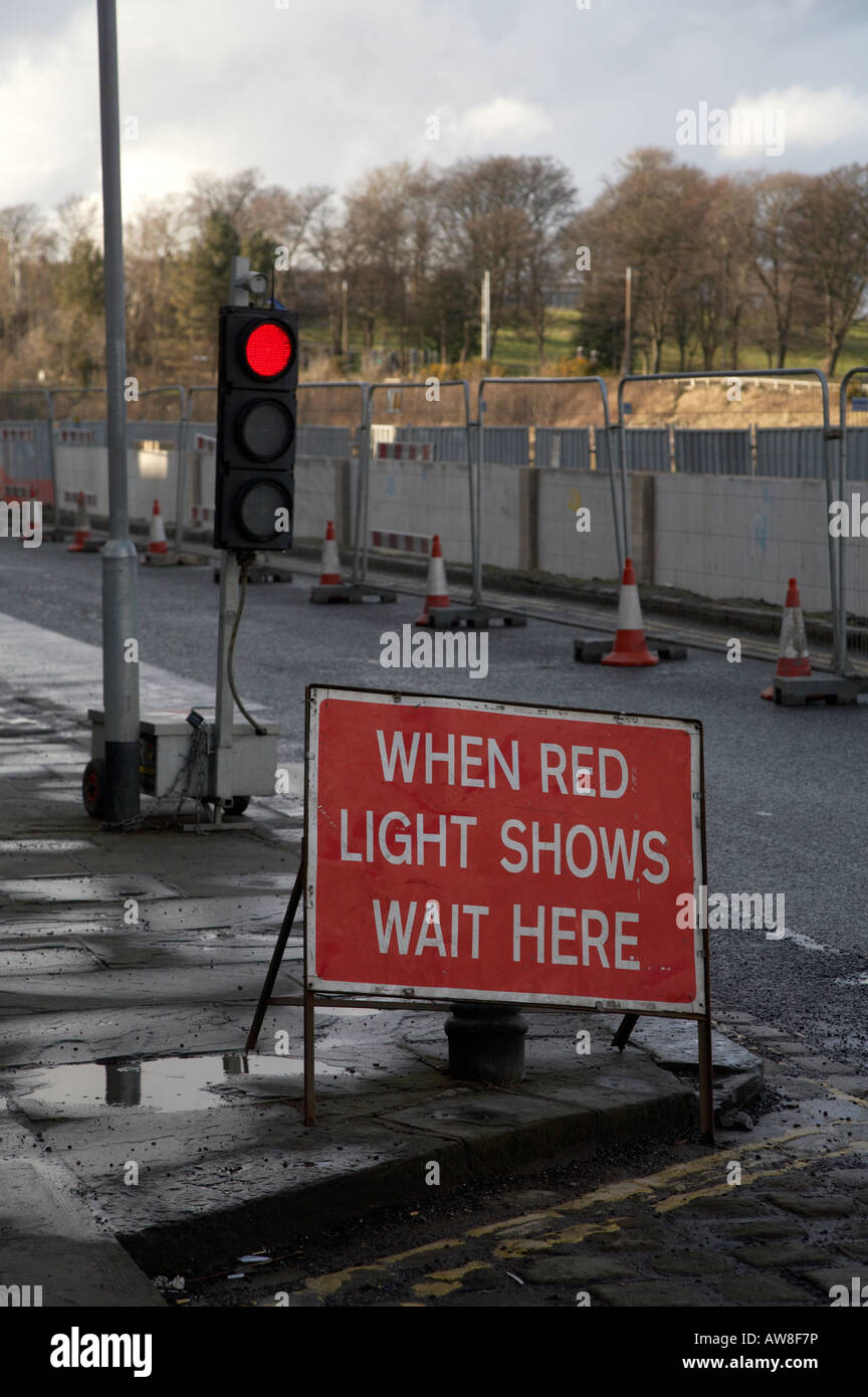 red temporary traffic light and sign saying stop here at road works