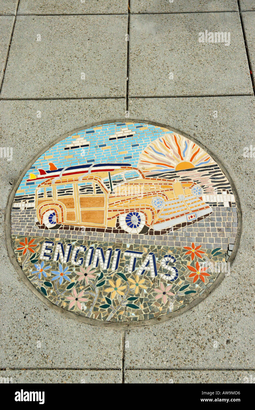A round mosaic tile decoration in the sidewalk shows Encinitas and a Woody car with surfboards in downtown Encinitas, California, USA Stock Photo