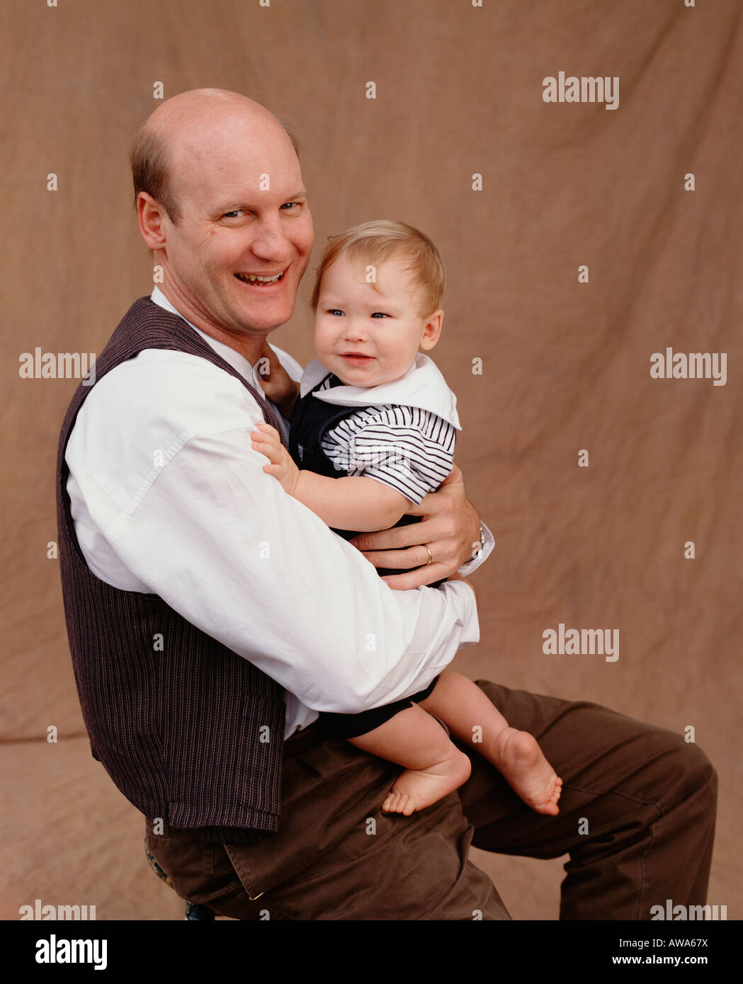 A studio portrait of a man holding his baby boy, with a big smile Stock Photo