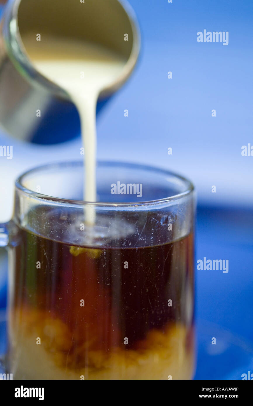 Sequence of pouring milk from a stainless steel jug into a glass of tea