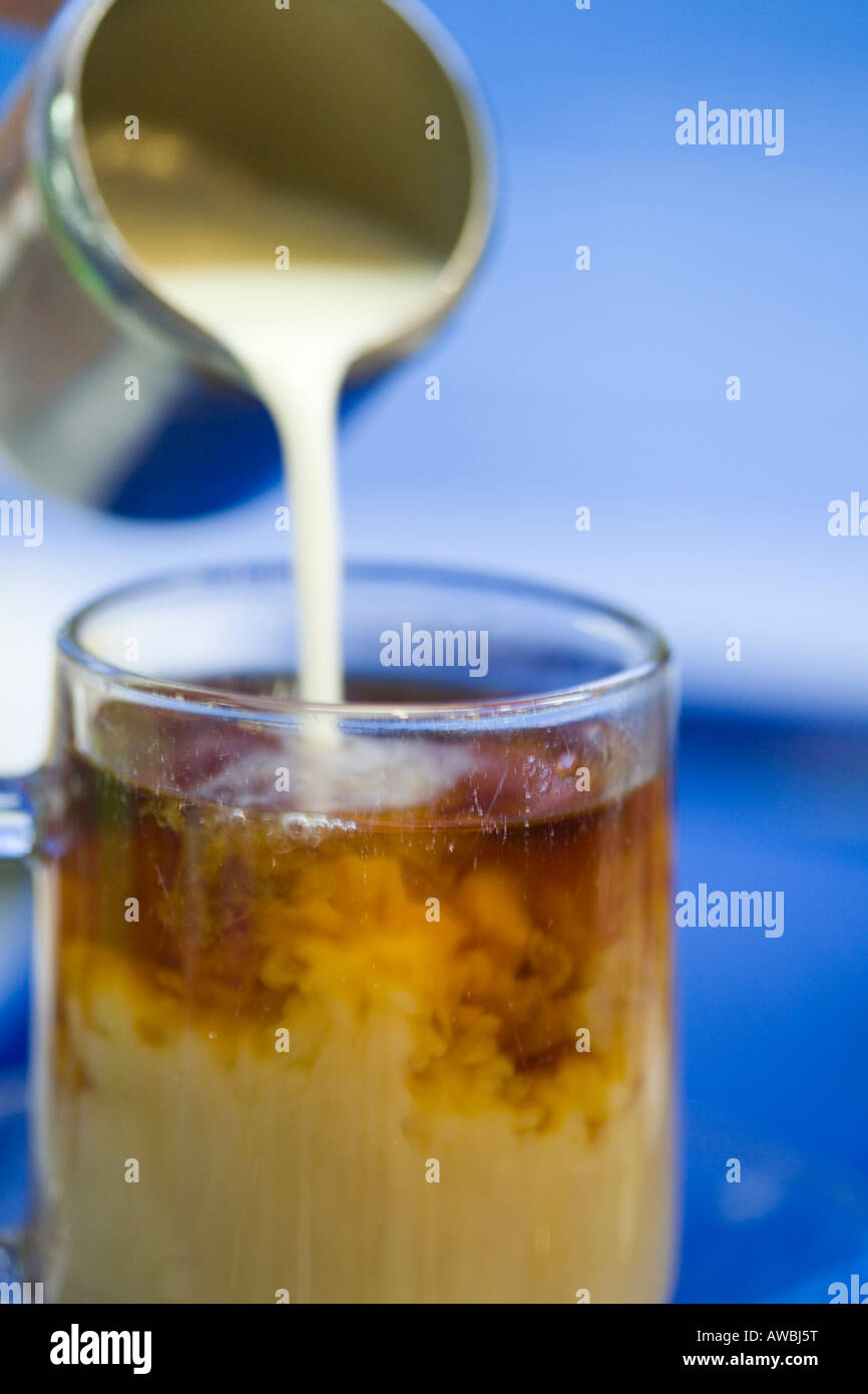 Sequence of pouring milk from a stainless steel jug into a glass of tea