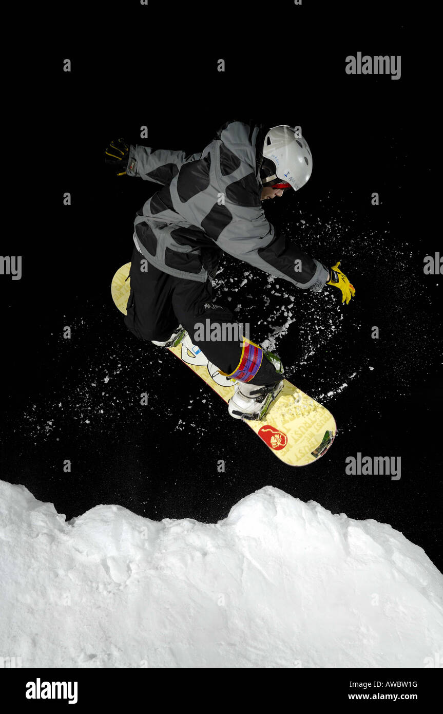 A young male snowboarder performs a freestyle stunt at night Stock Photo