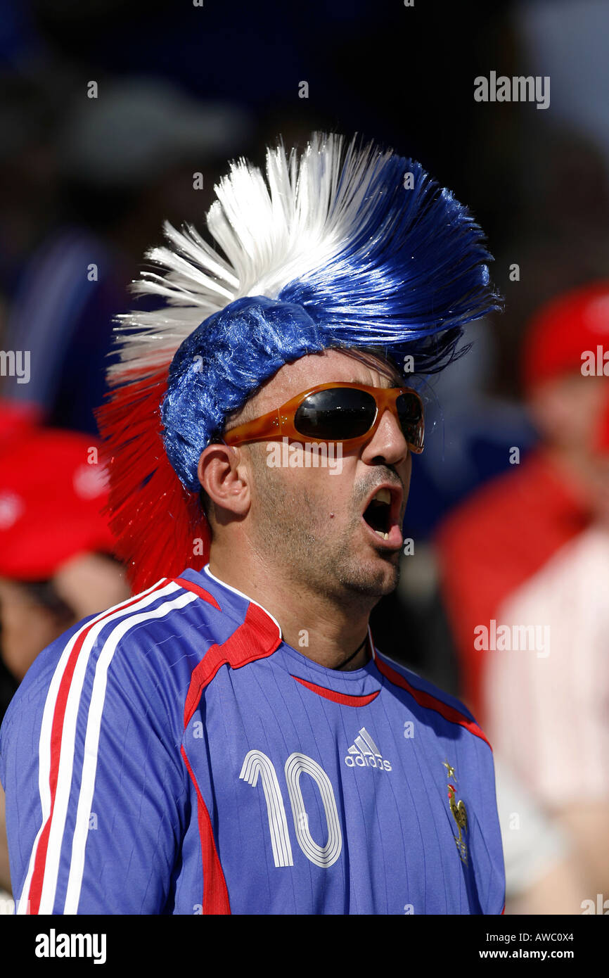 A male French fan wearing a mohican wig and sunglasses sings in the crowd during the 2006 World Cup Stock Photo