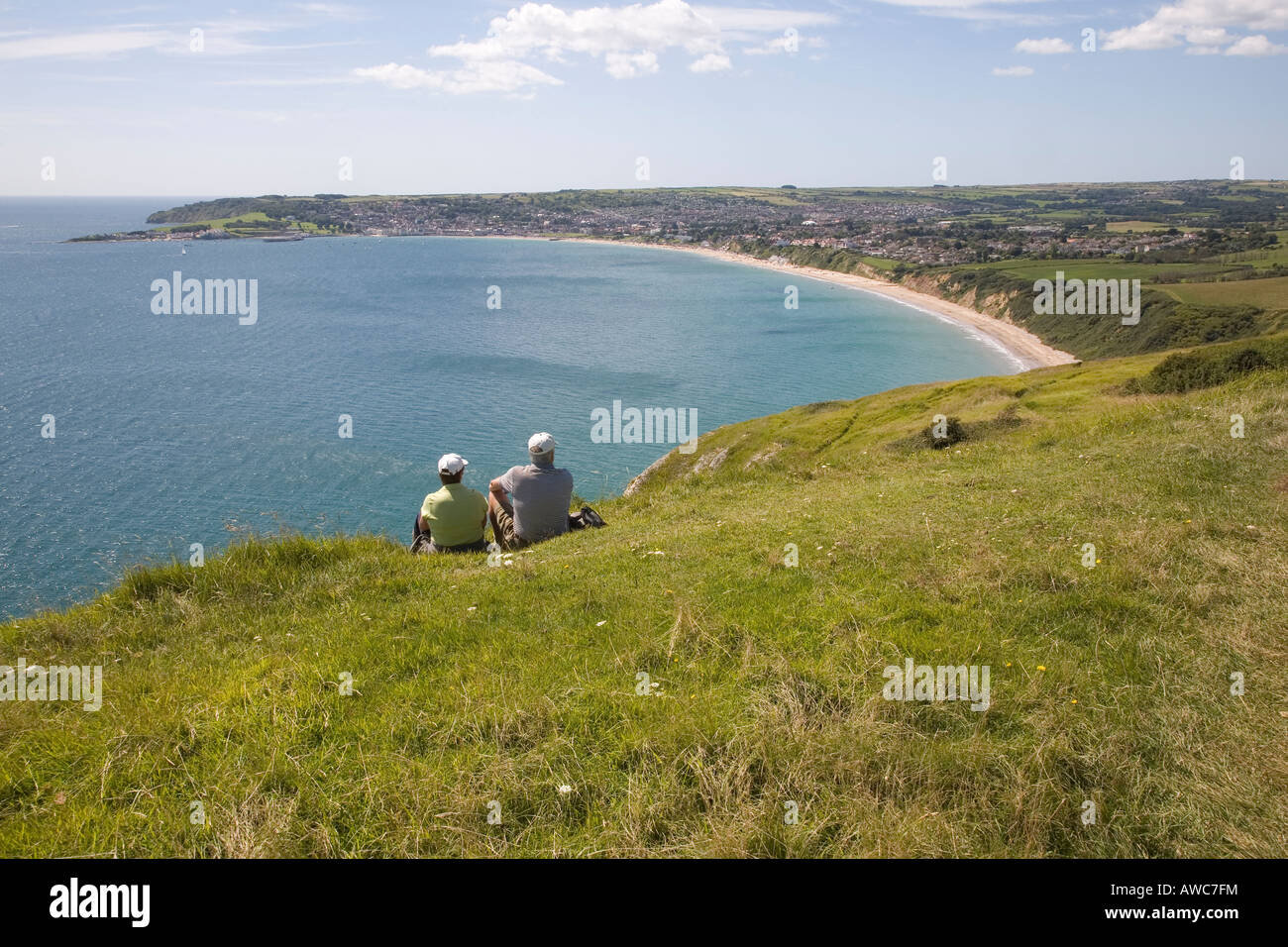 Couple sat on cliff top looking out over Swanage Bay Dorset UK Stock