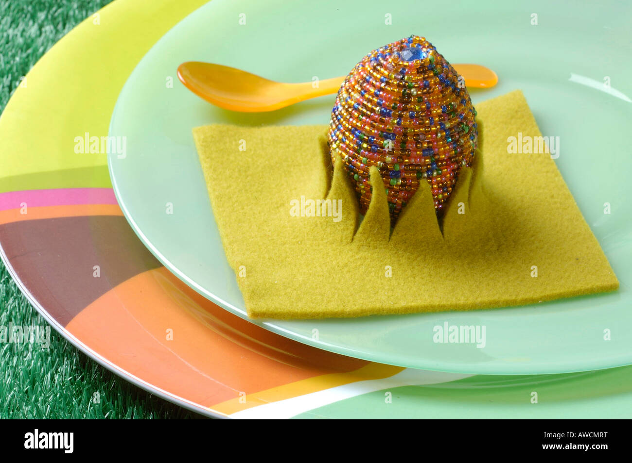 Colourful Easter egg with beads in felt cup on green and coloured plate Stock Photo