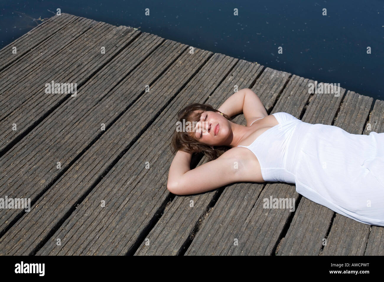 Woman in a white dress lying on a boardwalk enjoying the sun Stock Photo