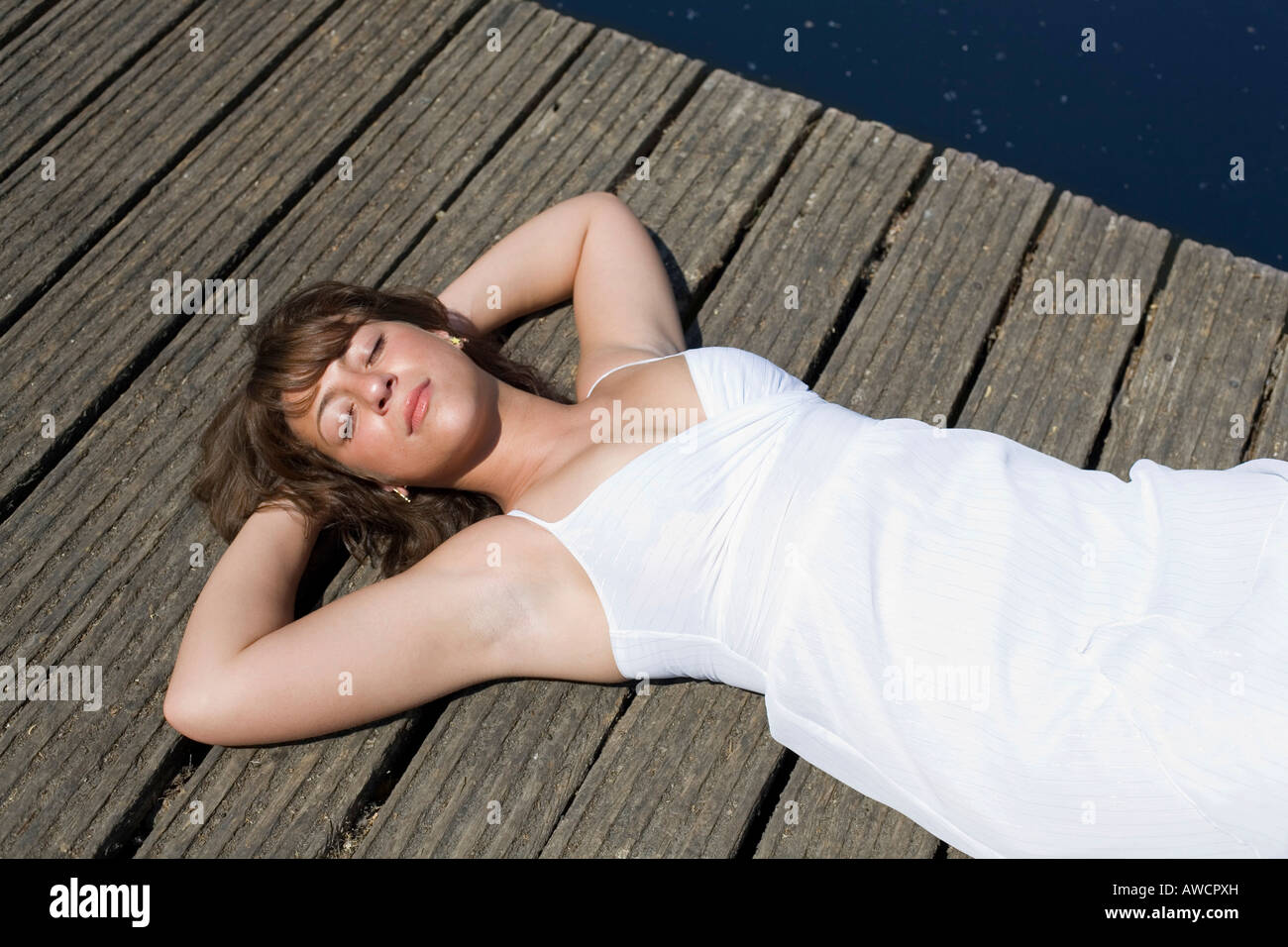 Woman in a white dress lying on a boardwalk enjoying the sun Stock Photo