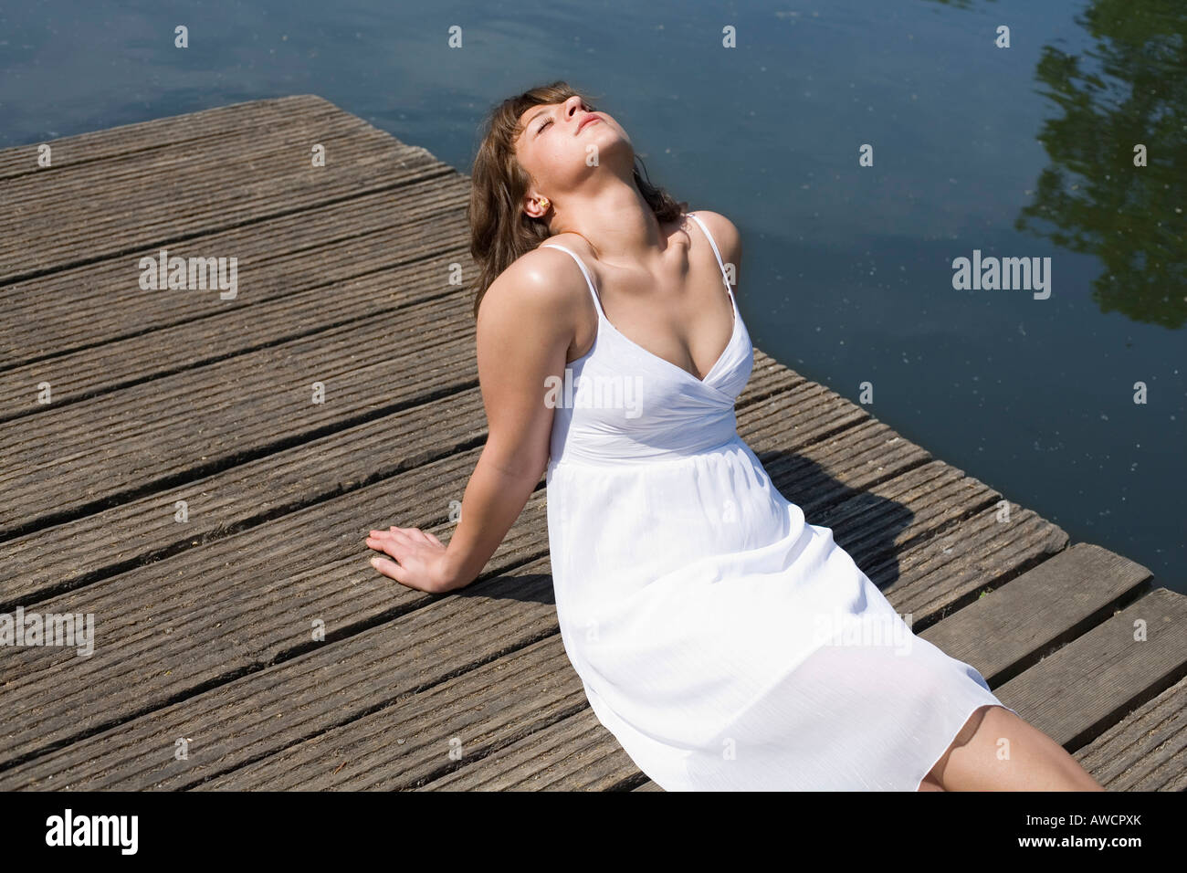 Woman in a white dress sitting on a boardwalk enjoying the sun Stock Photo