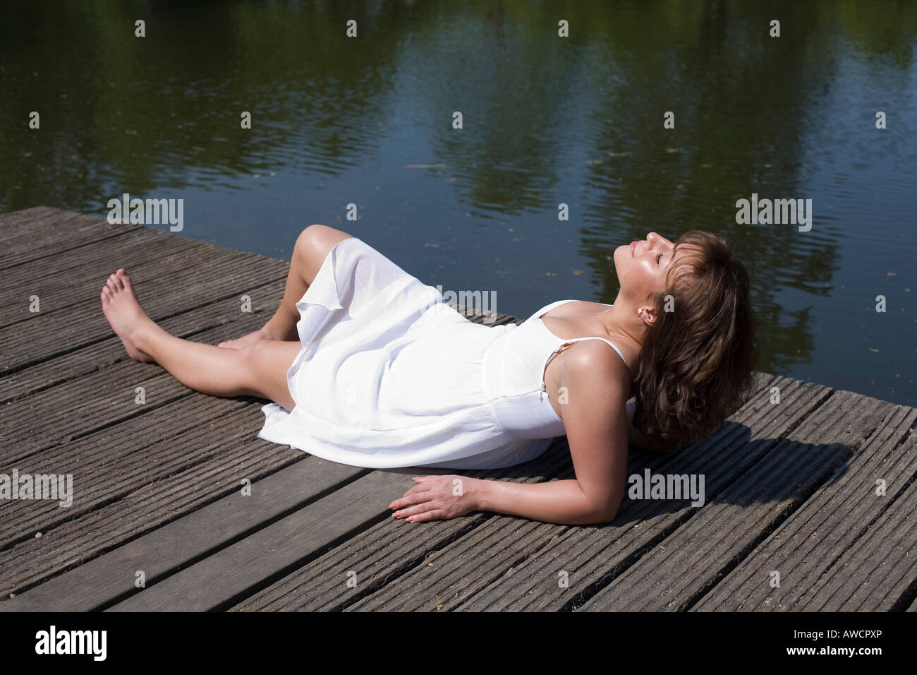 Woman in a white dress lying on a boardwalk enjoying the sun Stock Photo