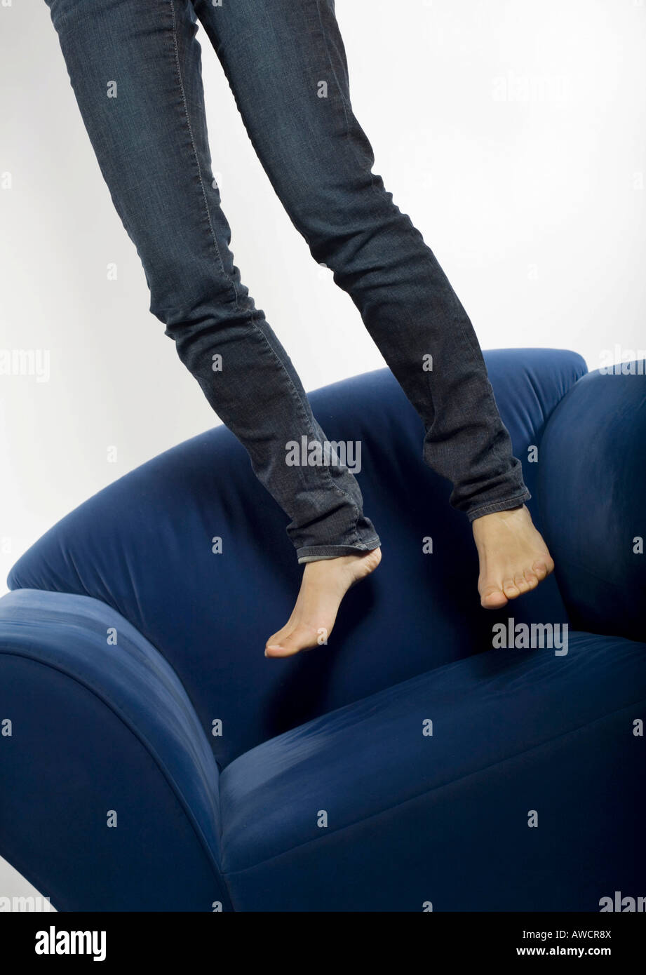 Woman in jeans jumping barefooted on a blue armchair Stock Photo