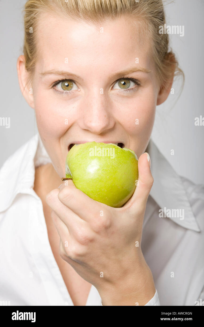Young blond woman biting into a green apple Stock Photo