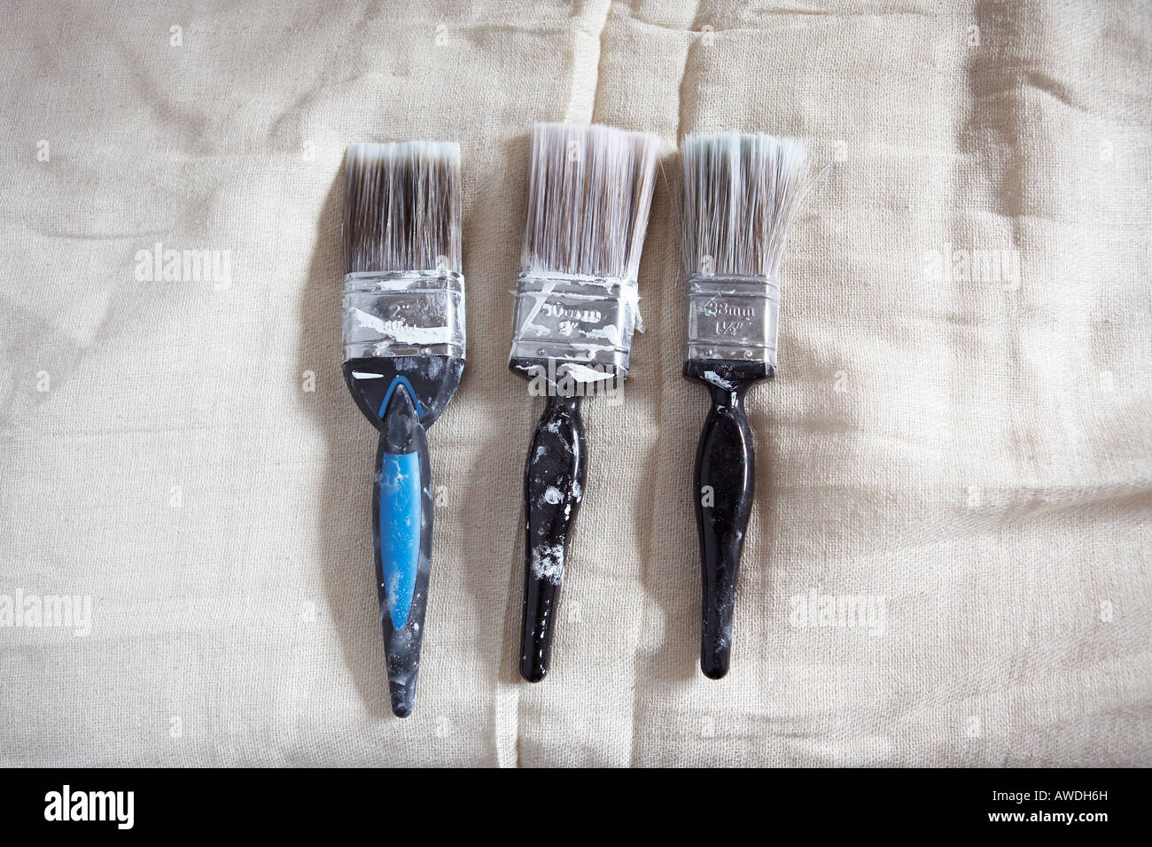 Row of three used paintbrushes on dust sheet Stock Photo