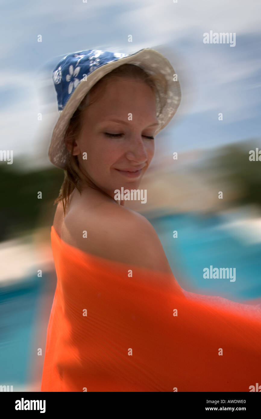 Teenage girl wearing sunhat wiping her back with an orange beach towel. Suntan. Lotion. swimming. Stock Photo