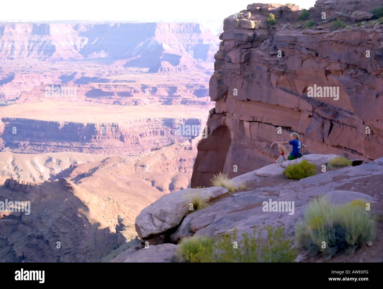 A young man sits casually near the cliff edge, with a grand vista below, in Dead Horse National Park in southern Utah, USA. Stock Photo