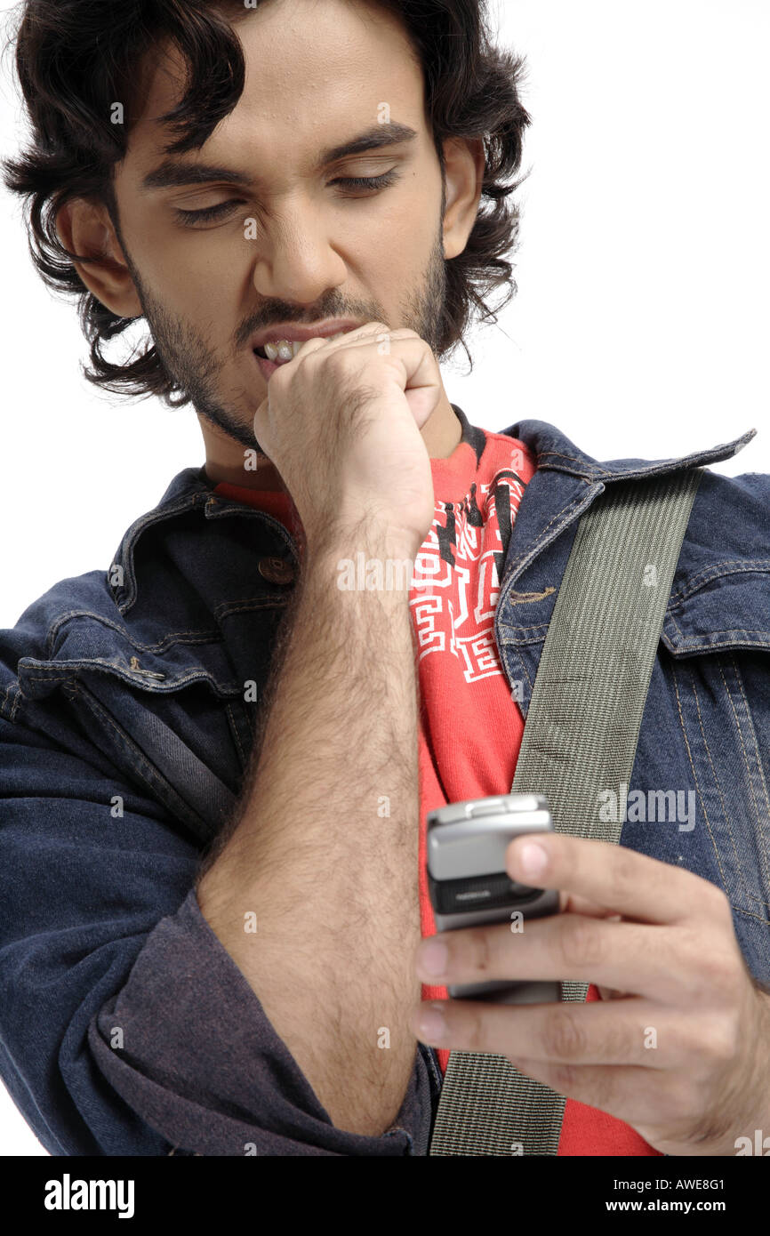 ANG200394 Teenage boy with beard and moustaches looking at mobile touching his teeth with right hand thinking MR 687T Stock Photo