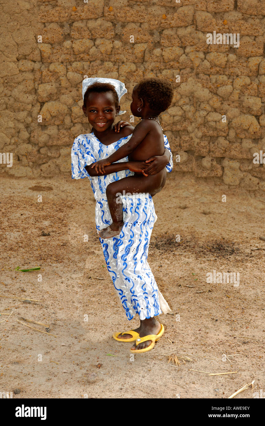 Young African girl carries her sister on the arm, village scene in Burkina Faso Stock Photo