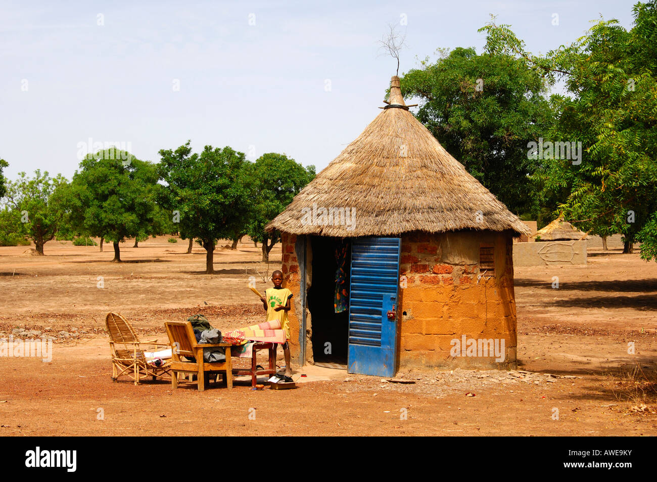 African round hut with thatched roof and interior furniture placed outside during household clean-up, Burkina Faso Stock Photo