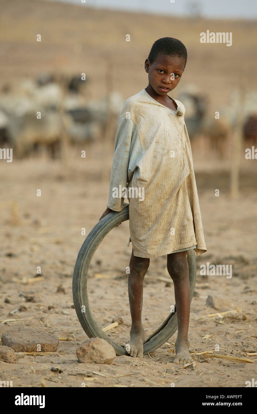 Boy leaning against an old tire in front of a herd of Zebus, Sahel region, Cameroon, Africa Stock Photo