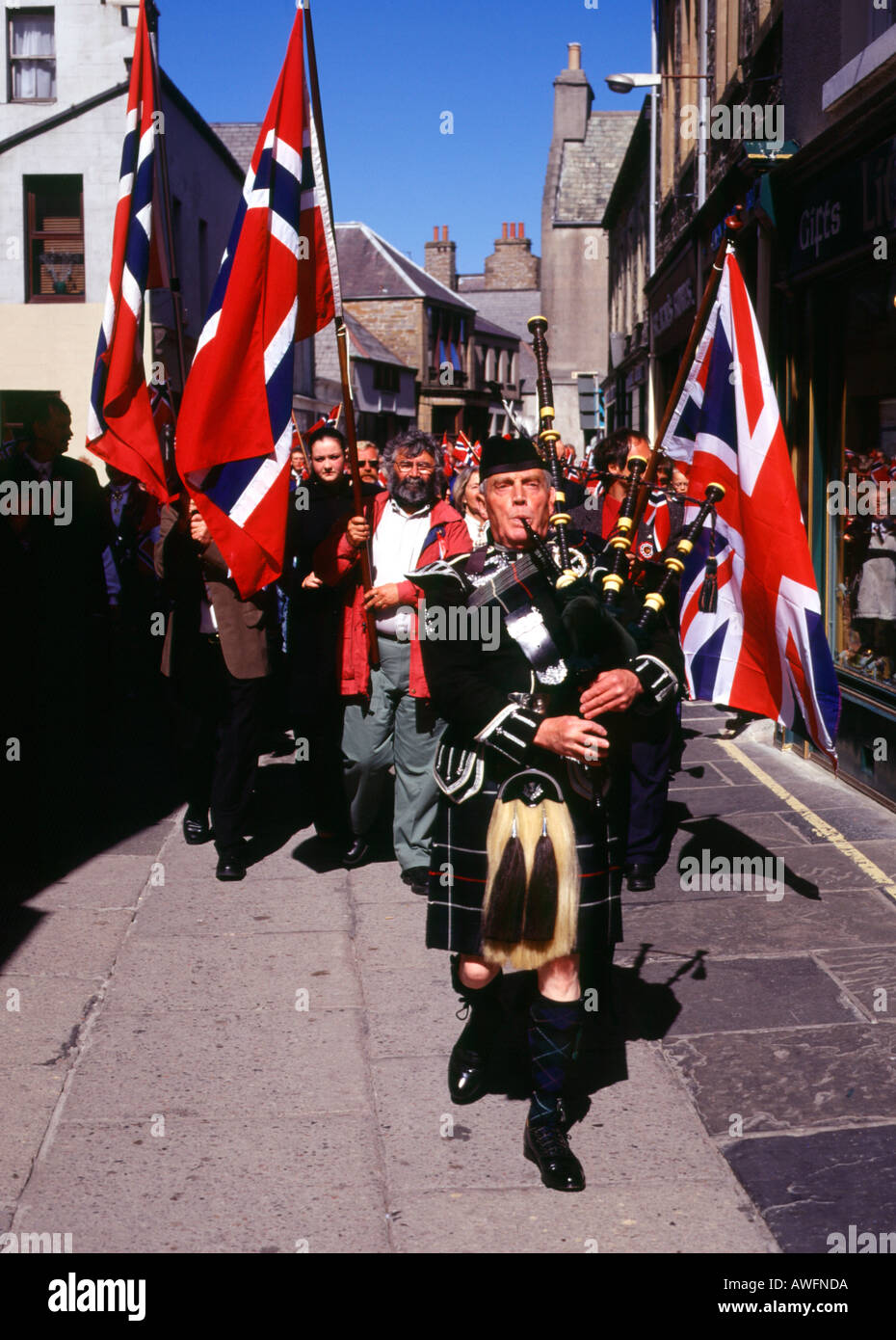 dh Norwegian Constitution Day KIRKWALL ORKNEY Bagpiper leading street parade Albert street Flags procession piper scottish national dress Stock Photo