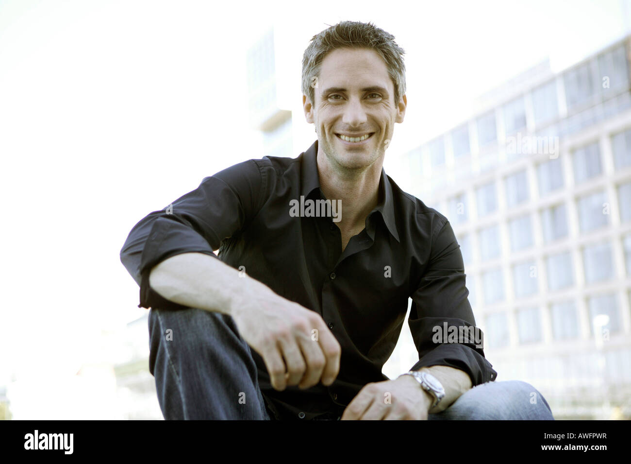 Young man in black shirt in front of high-rise building Stock Photo