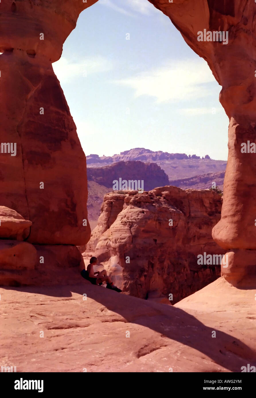 A lone hiker rests from his arduous hike & the unrelenting summer heat underneath Delicate Arch in the red rock country of UT. Stock Photo