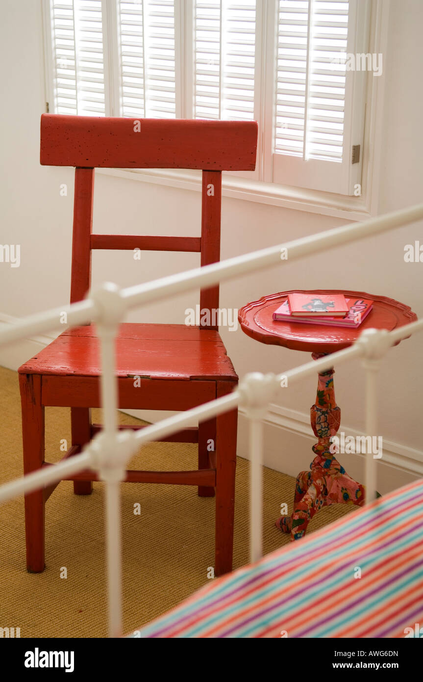 Red wooden chair and circular table at foot of wrought iron bed Stock Photo