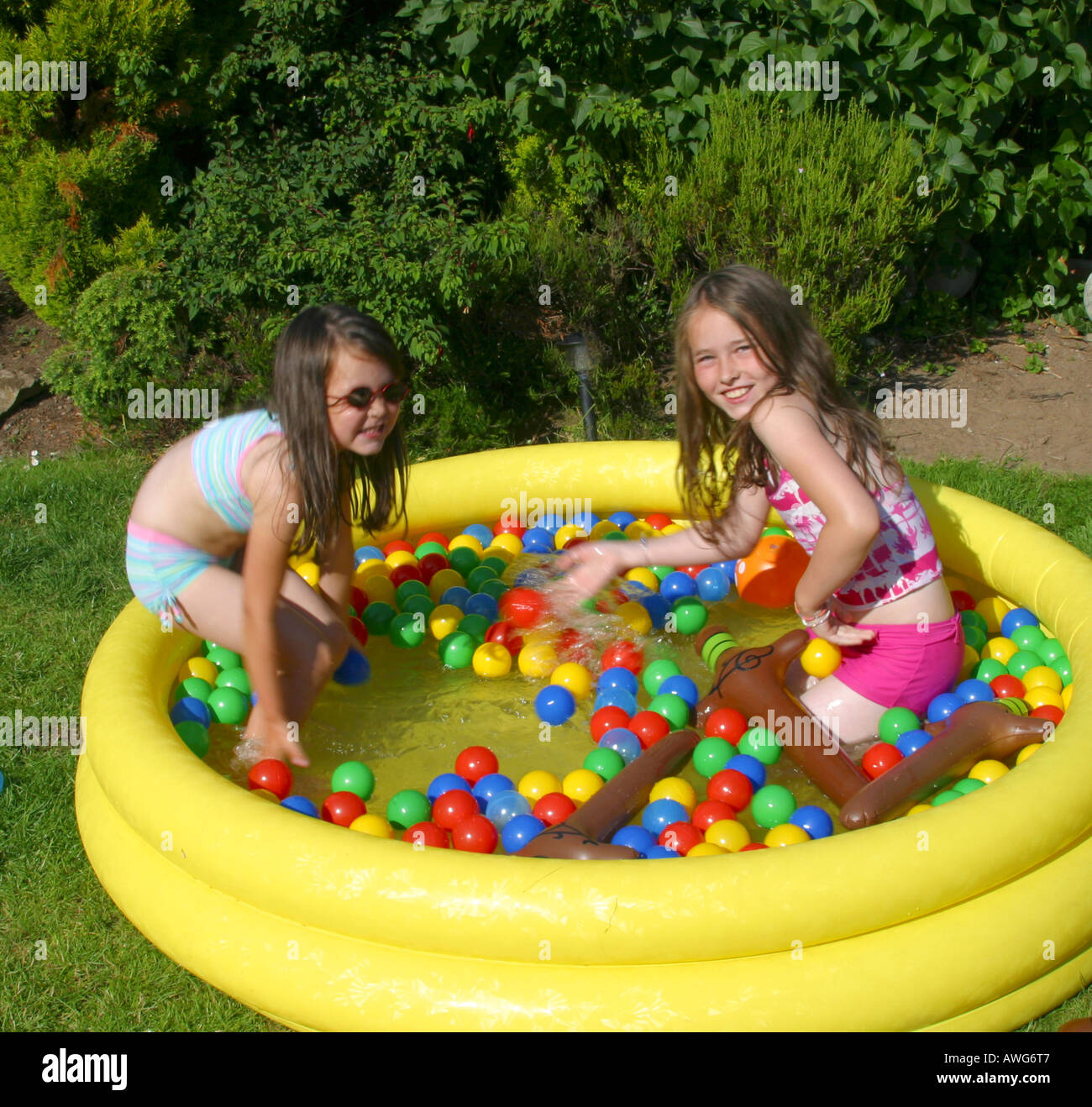 Two young girls playing in paddling pool in  garden Stock Photo